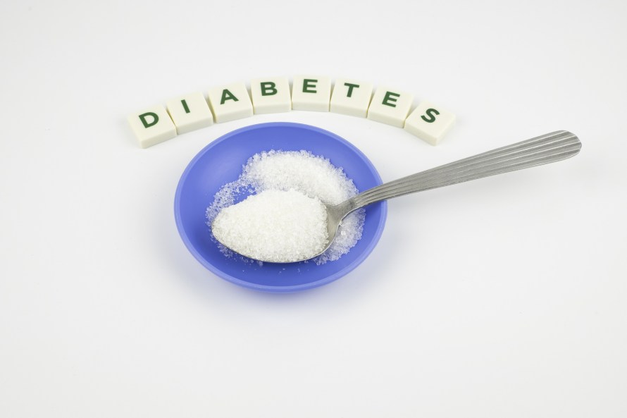 Diabetes word in crossword style block letters and spoon or teaspoon with white sugar in health care and healthy nutrition concept over white background