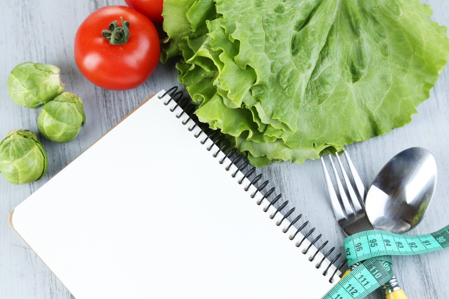 Cutlery tied with measuring tape and notebook with vegetables