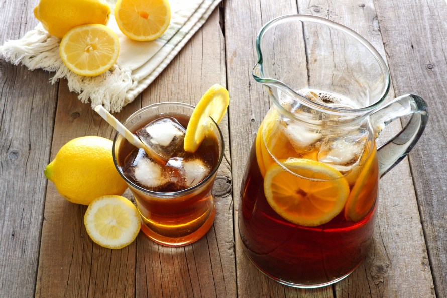 Pitcher of fresh lemon iced tea with filled glass on a rustic wooden background