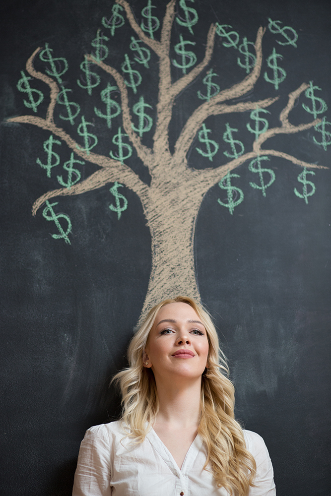 Happy blonde Business woman in front of chalk money tree drawing on blackboard.