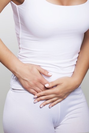 Stomach ache. Painful sensations on the right side of the abdomen. Appendicitis. Young woman holding hands on her stomach. The concept of health. On a gray background.
