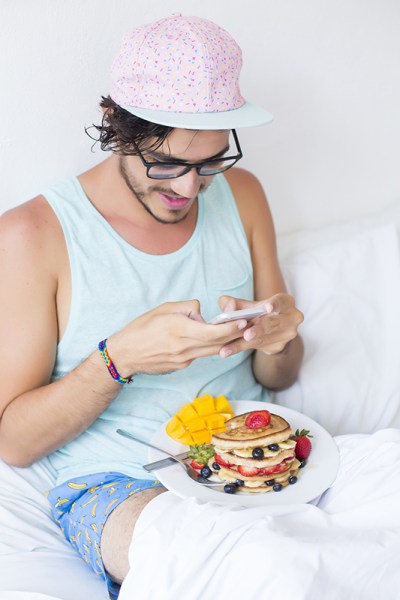 Young man having pancakes in bed