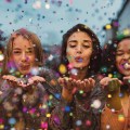 Young women blowing confetti from hands. Friends celebrating out
