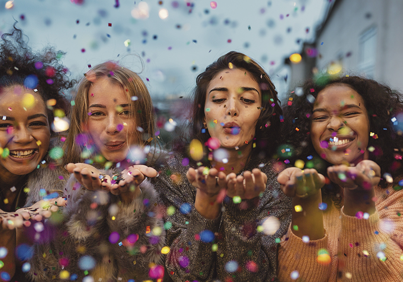 Young women blowing confetti from hands. Friends celebrating out