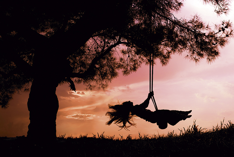 silhouette of happy young woman on a swing with sunset background