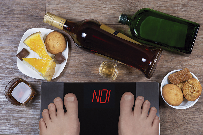 Male feet on digital scales and sign no surrounded by bottles an